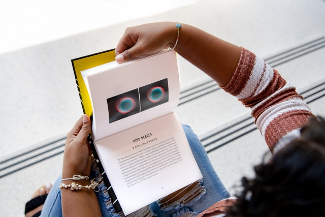 hands holding an open book showing interior pages with images of the galaxy