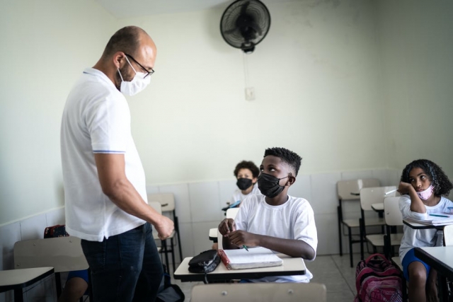 teacher talks with student sitting at a desk