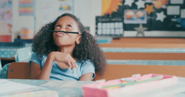 Student playing with pencil at a desk in a classroom